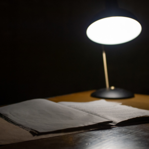 Set with a dark background, this picture shows a slightly blurred desk lamp shining onto an open file folder atop a wooden desk