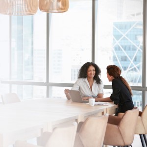 two women at board table with laptop smiling and discussing