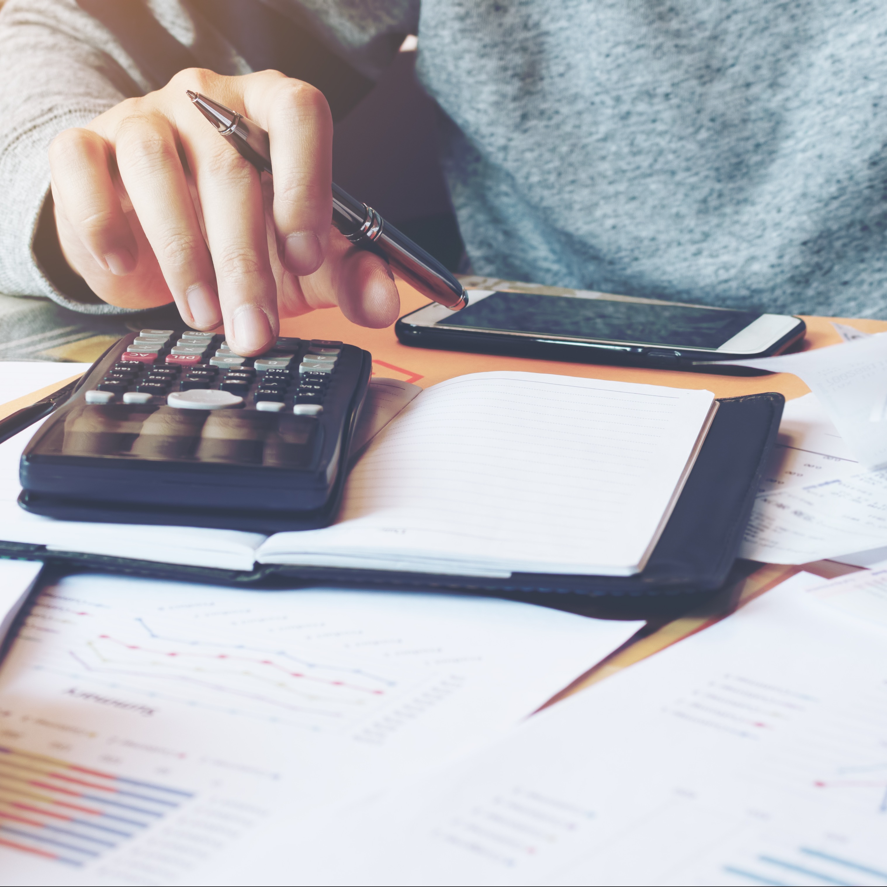 Picture of man's hand working on calculator with papers and cell phone laying on desk