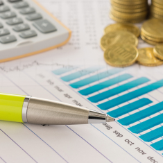 Picture of pen, money and calculator laying across block graph and financial print out