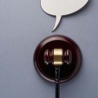 Brown wooden gavel with a gold band on the hammer part of the head, resting on a round platform; a white speech bubble sits above the gavel; 