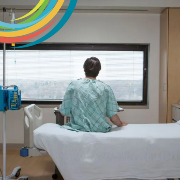 Picture of the back of a man looking out a window. He is sitting on hospital bed.