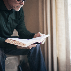 Man with glasses sitting on chair reading Bible