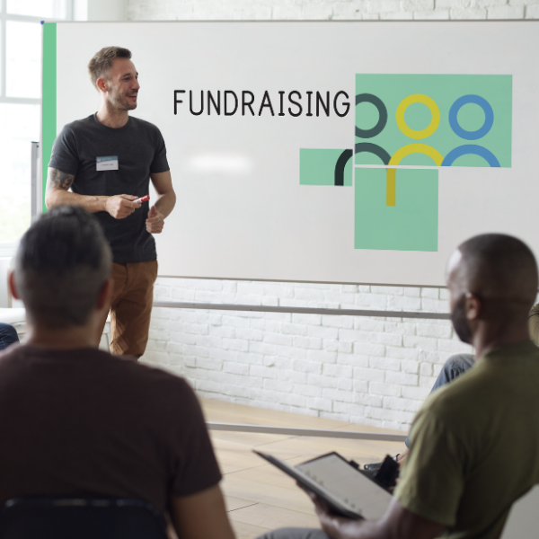 Man standing at front of room beside whiteboard with the words fundraising