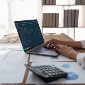 Picture of hands working on laptop at desk with calculator and papers