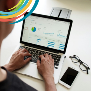 Picture of desktop with glasses, phone and open laptop with person's hands working on laptop