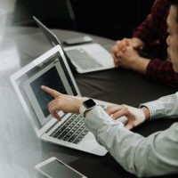 Man working on a laptop and another employee watching