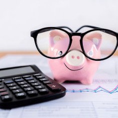 Picture of desk with calculator, financial statements and piggy bank with glasses