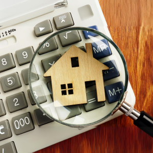 A magnifying glass on top of a wooden cut out of a house, on top of a keyboard