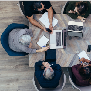 Five business colleagues gathered around meeting table with laptops and paper