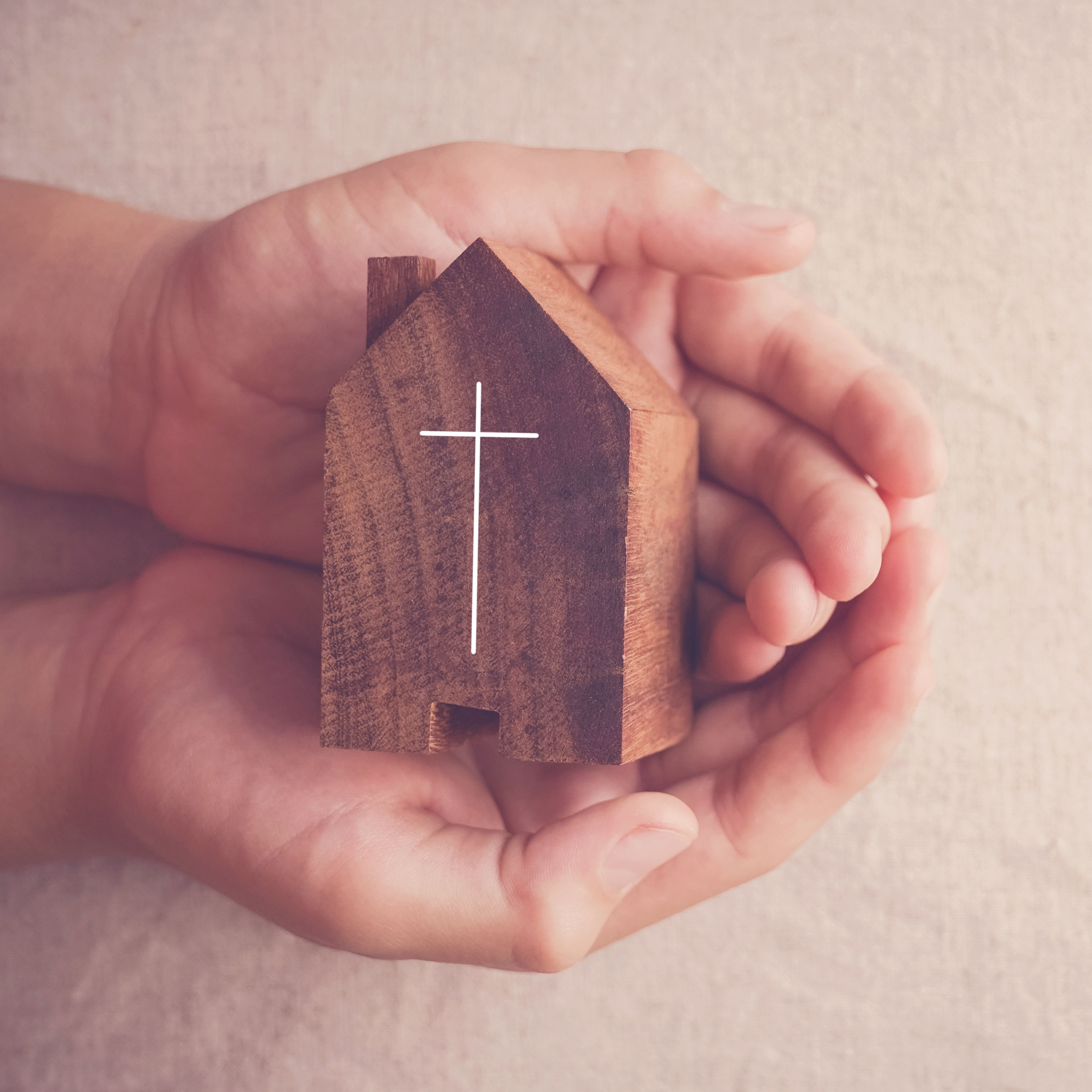 Picture of hands holding wooden building with cross on it