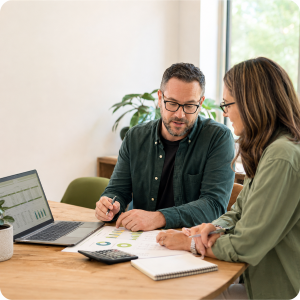 Two people (man and woman) sitting at a table looking at papers and laptop