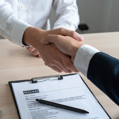 Two hands shaking above desk that has a resume placed on it.