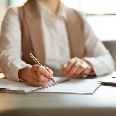Mother holding her baby while sitting at table writing on notepad with laptop open