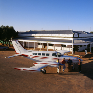 Picture of small airplane on tarmack with people standing outside of plane and building in background