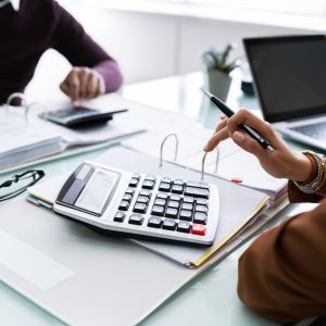 Picture of two employees working at a desk with calculator and laptop