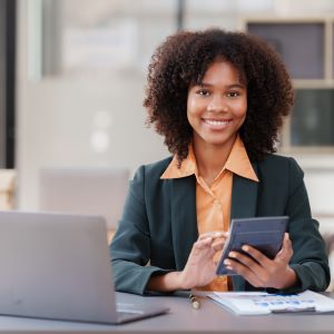 Picture of smiling woman sitting at desk working on calculator with laptop