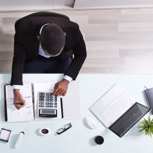 Picture of man at desk with laptop, calculator and paper documents