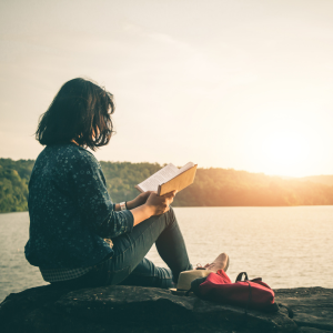 Women sitting next to lake, reading a book