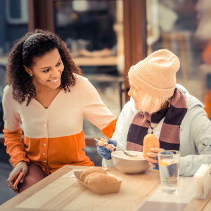Young woman sitting with elderly woman at table and young woman has her hand on senior woman shoulder