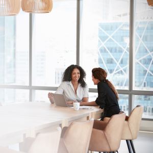 Picture of two smiling women sitting at table with laptop 