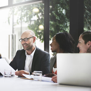 3 Work Colleagues sitting at table with papers and laptop