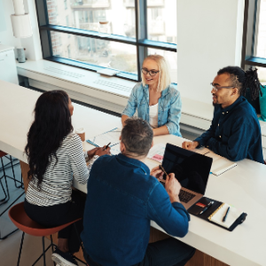 Group of 4 smiling colleagues - 2 females and 2 males - talking and sitting at meeting table 