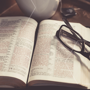 Picture of open Bible laying on table with glasses set on top of Bible