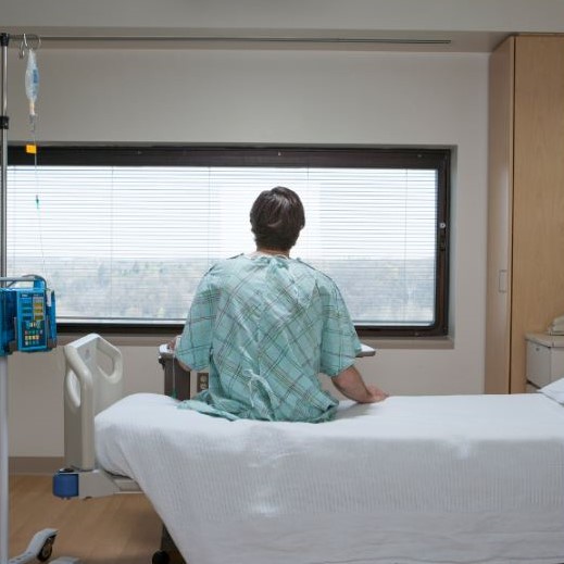Man in hospital gown sitting on hospital bed looking out window