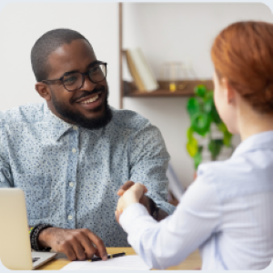 Picture of smiling man seated at desk shaking hands with woman on other side of desk