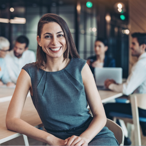 Smiling professional woman with group of colleagues in background sitting around board table