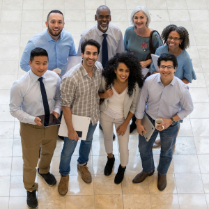 Smiling group of 8 work colleagues looking up at camera and smiling