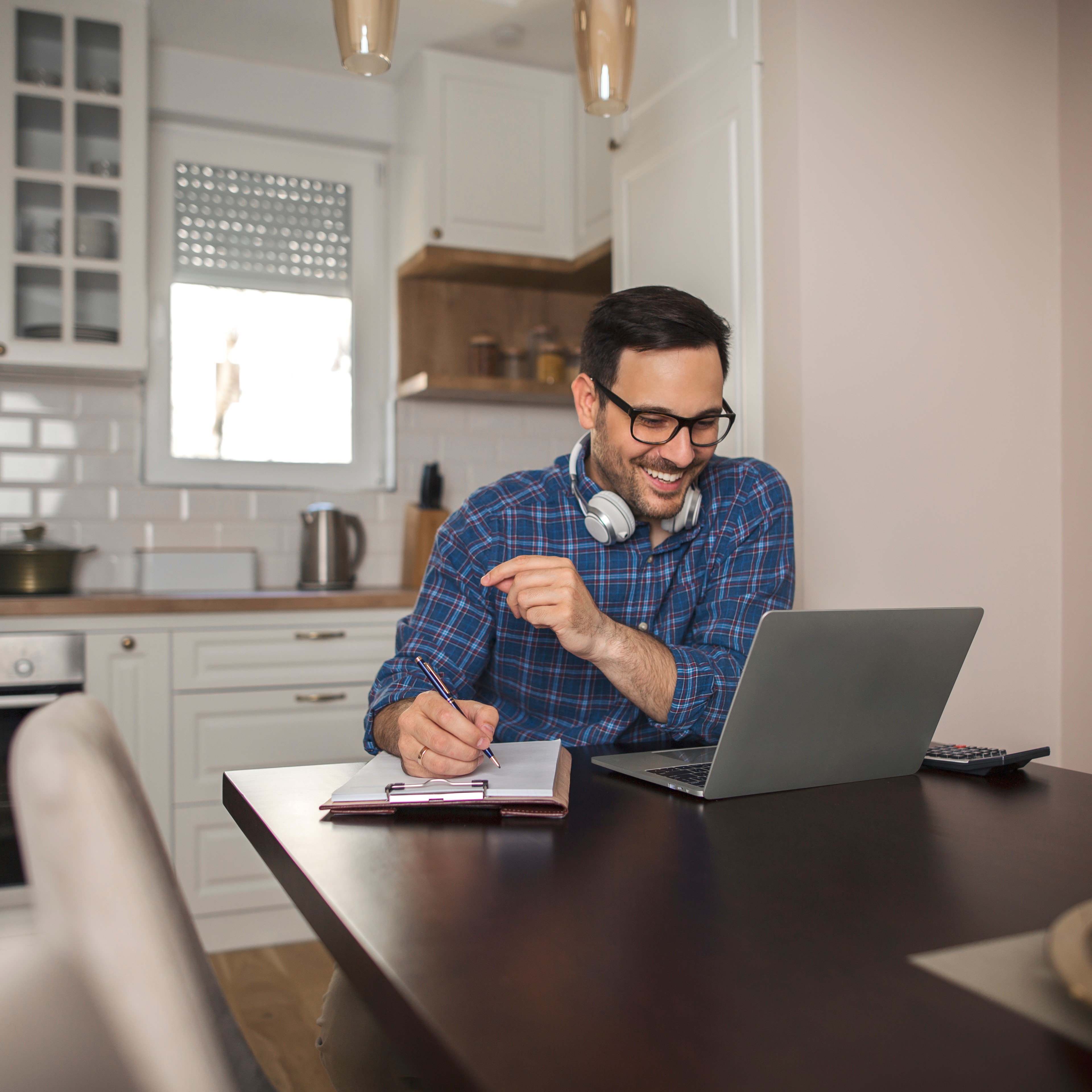 Smiling man at kitchen table with laptopm calculator and paper