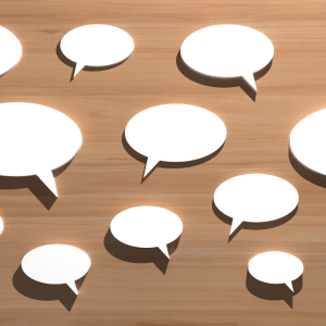 White cut-out speech bubbles of various sizes in front of a wood coloured background