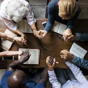 people studying bible, praying, holding hands