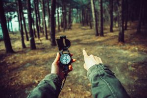 man holding compass in a forest pointing in the direction to go