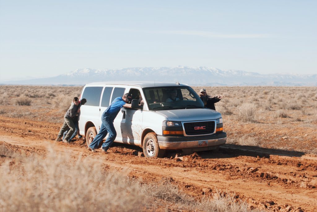 Van stuck in the mud being pushed by people