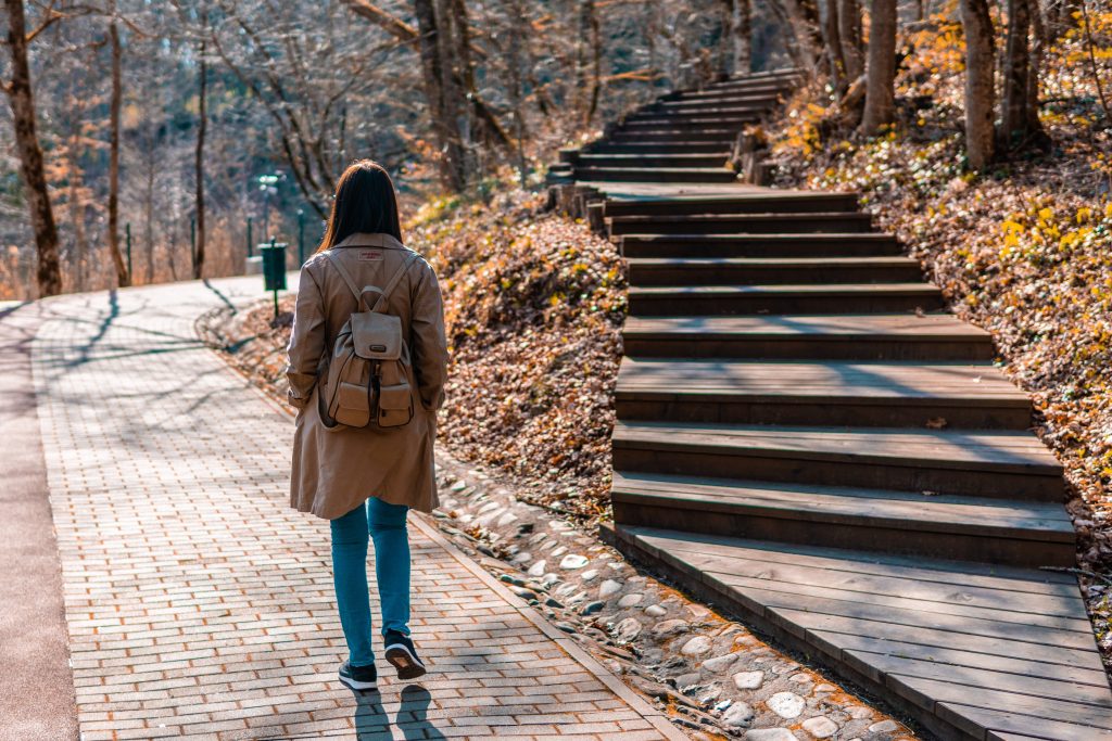 Person walking on a wide brick path passing by wooden stairs leading up to the rightden stairs leading uphill to the right.